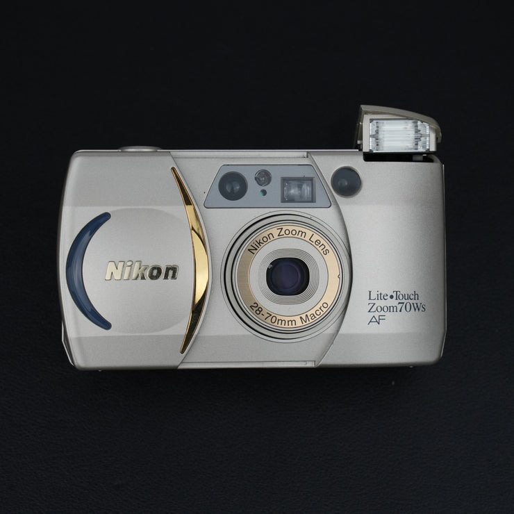 Fotocamera con sportellino aperto, visibile l’obiettivo zoom 38–70mm f/4.5–8.