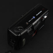 ista dall’alto della fotocamera Olympus AF-10 Super, con pulsante di scatto, flash e selettore modalità.