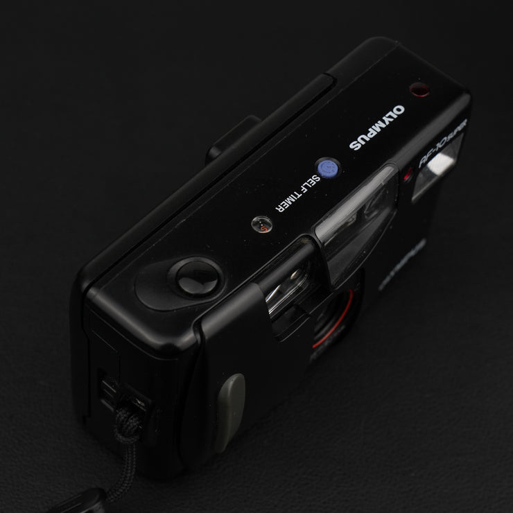ista dall’alto della fotocamera Olympus AF-10 Super, con pulsante di scatto, flash e selettore modalità.