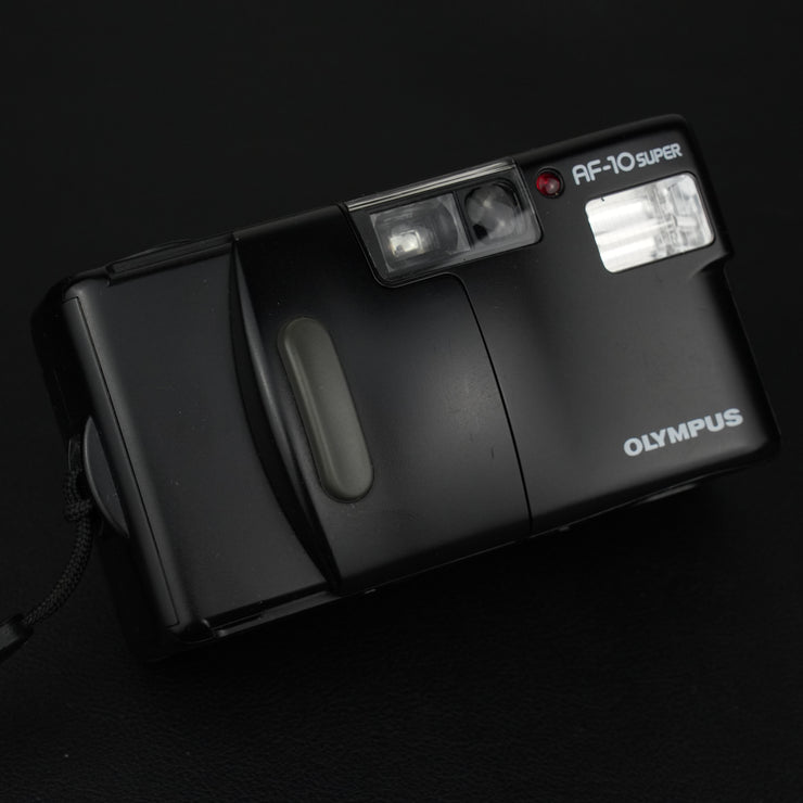 Vista frontale della fotocamera Olympus AF-10 Super con sportellino chiuso, design compatto e linee pulite.