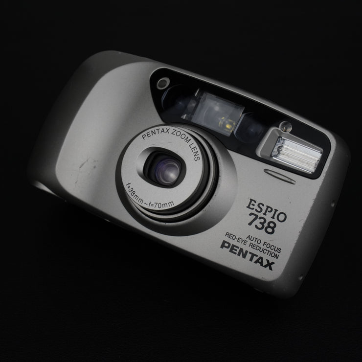 Fotocamera con sportellino aperto, visibile l’obiettivo zoom 38–70mm f/4.5–8.