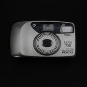 Vista frontale della fotocamera Pentax Espio 738 con sportellino chiuso e design compatto.