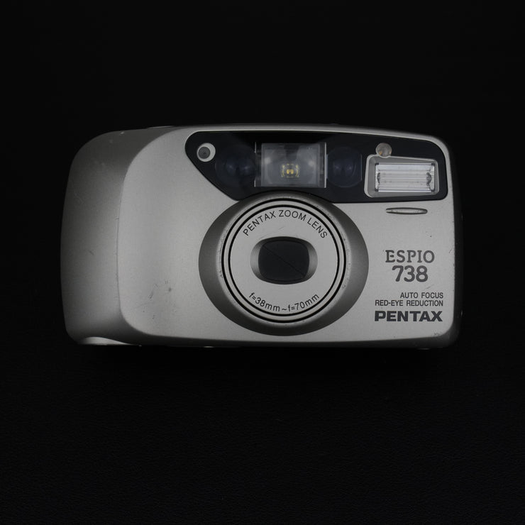 Vista frontale della fotocamera Pentax Espio 738 con sportellino chiuso e design compatto.