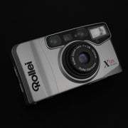 Fotocamera con sportellino aperto, visibile l’obiettivo zoom 38–125mm f/4.6–12.2.