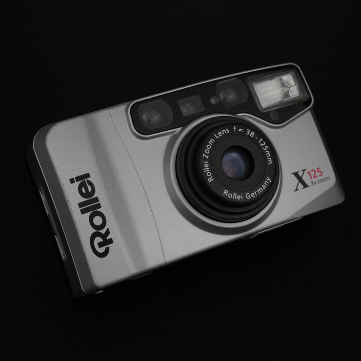 Fotocamera con sportellino aperto, visibile l’obiettivo zoom 38–125mm f/4.6–12.2.