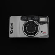 Vista frontale della fotocamera Rollei X125 con sportellino chiuso e design compatto.