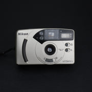 Fotocamera Nikon AF240SV frontale con copriobiettivo aperto, obiettivo fisso 28mm