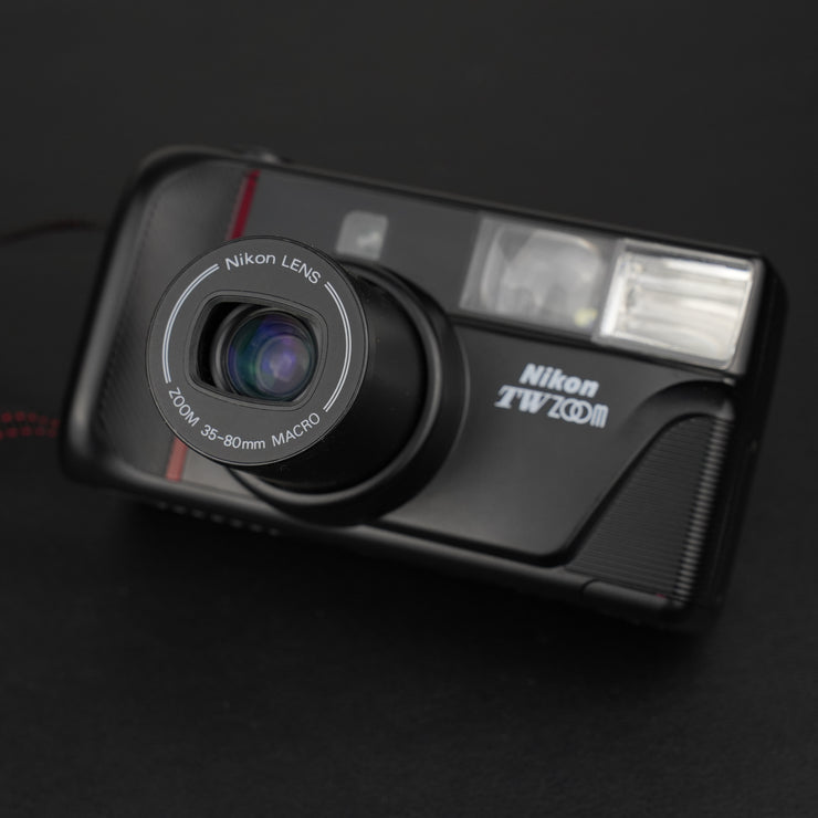 Fotocamera analogica Nikon TW Zoom frontale con sportellino aperto e obiettivo in estensione.